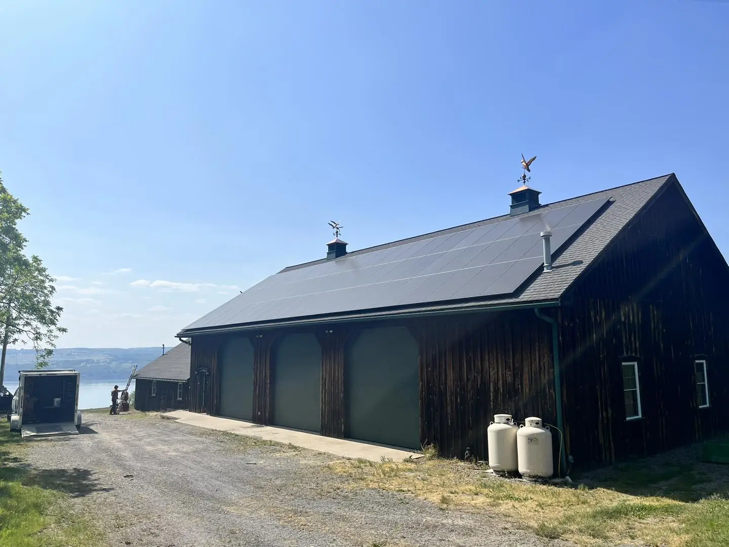 Dark wooden barn with solar panels installed on sloped roof near lake